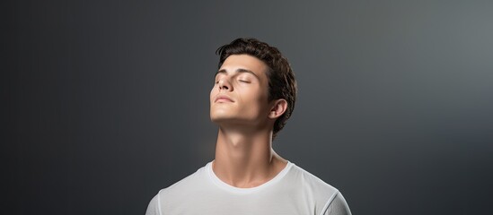 Obraz premium Studio portrait of a thoughtful young man in a white t shirt He presses his lips together hard and looks up Isolated large image on grey background. copy space available