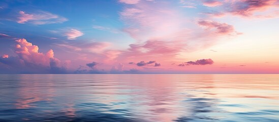 Obraz premium Idyllic seascape at sunset with a clear blue sky and colorful glowing pink clouds The soft light creates symmetry reflections on the water acting as a natural mirror with a textured surface This imag