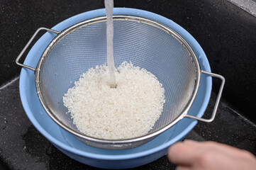 Myć ryż, ziarna bialego ryzu rzed gotowaniem na durszlaku z bliska