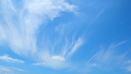 A clear blue sky adorned with ethereal, wispy clouds. The clouds have a feather-like appearance,...