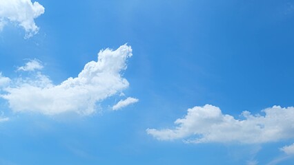 A bright blue sky with a few fluffy white clouds. The clouds have a distinct, billowy appearance,...