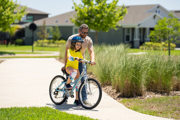 Obraz premium Fathers day. Boy learning to ride a bicycle with his father in park. Father teaching his son cycling on bike. Father learn little son to ride a bicycle. Father support child. Fathers day background.