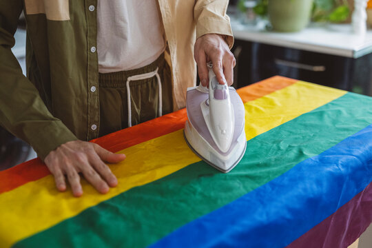 Non-binary person ironing rainbow flag at home