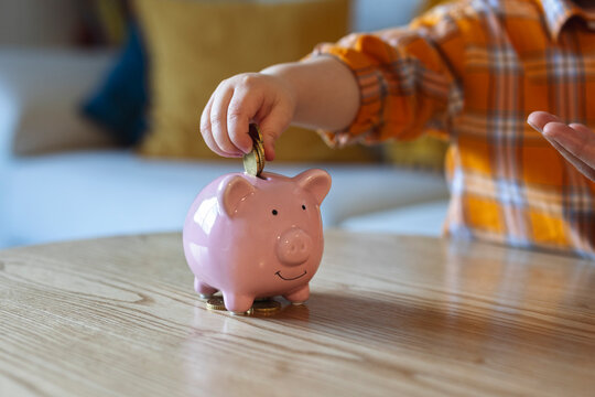 Boy putting coins in pink color piggy bank at home