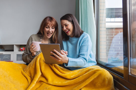 Cheerful sisters using tablet PC and relaxing at home