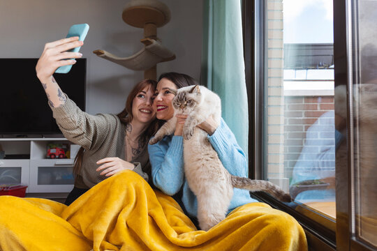 Smiling women taking selfie with cat through smart phone