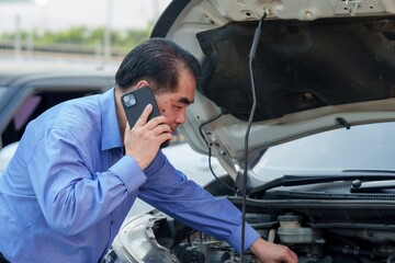 Insurance officer on phone while inspecting car engine. Asian man in shirt, Represents prompt...