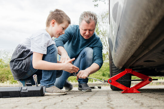 Son helping father installing car jack below car