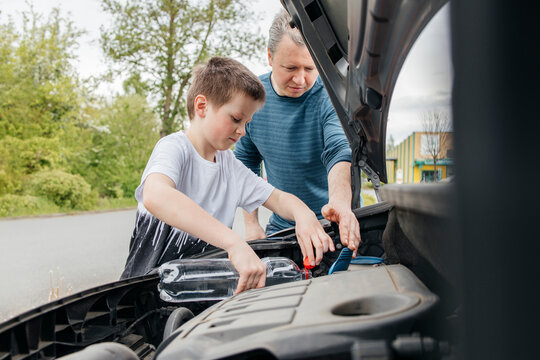 Father helping son pouring liquid into windshield wiper storage tank
