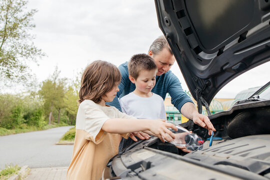 Children pouring liquid in windshield wiper storage tank by father