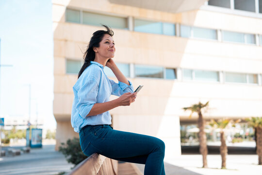 Smiling businesswoman with smart phone sitting on bench