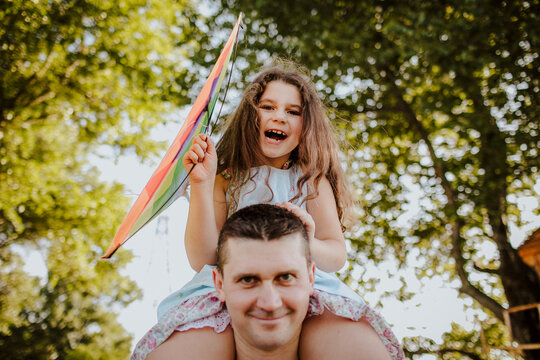 Happy girl sitting on father's shoulder flying kite at garden