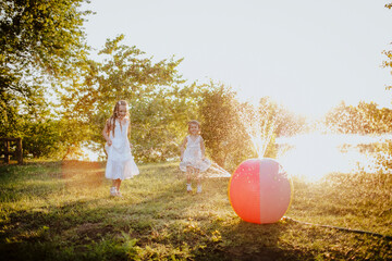 Siblings playing near colorful ball splashing water at garden