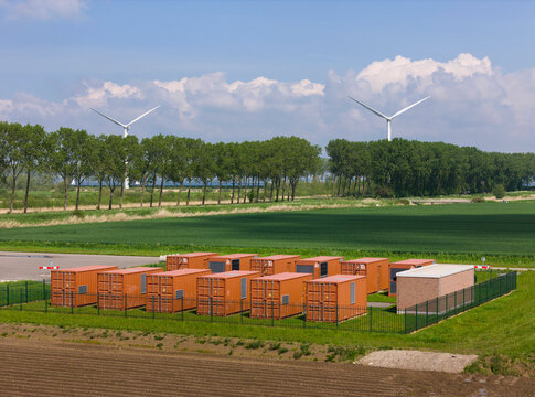 Huge red battery containers in front of trees and wind turbines