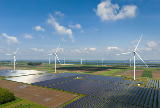 Solar panels with wind turbines on field under cloudy sky