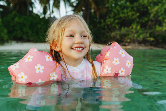 Smiling cute blond girl with water wings swimming in sea