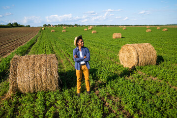 African farmer is standing in his agricultural field. He is cultivating clover and making bales of...
