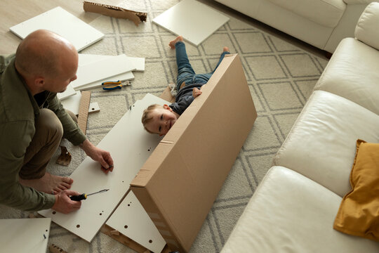 Father assembling furniture with son playing in living room at home