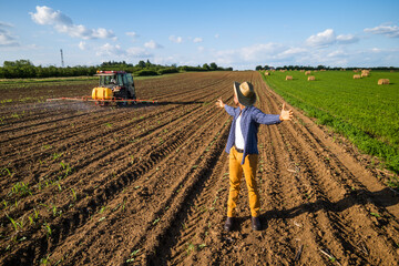 African farmer is standing in his agricultural field. He is supervising the spraying of the field.