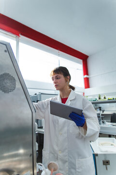 Young scientist using tablet PC examining bioreactor in laboratory