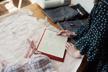 Detail of a fashion designer's hands sketching a new garment on pattern paper with fabric samples...