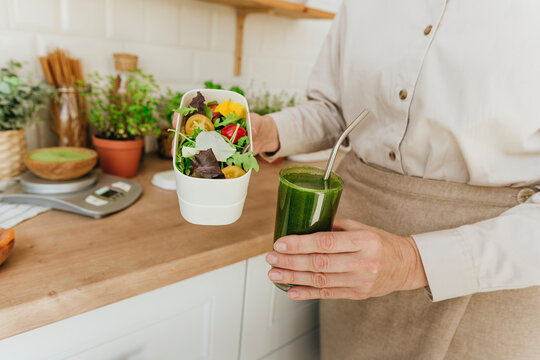 Woman holding salad and detox juice in kitchen at home