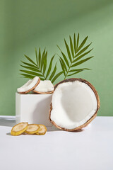 Photo was taken from front view on green background, a rectangular platform containing some pieces of coconut, next to a half of coconut and some banana slices, green coconut leaves decorated in back