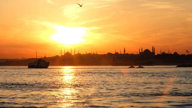 Istanbul, silhouettes of the sultanahmet mosques, Saint Sophia (Ayasofya), and a boat sailing on the Bosphorus, outlined by a magnificent sunset.