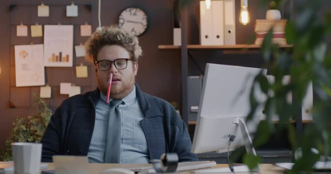 Loop portrait of silly employee sitting in office with pen in nose and relaxing in chair in evening. Businessperson and fun concept.