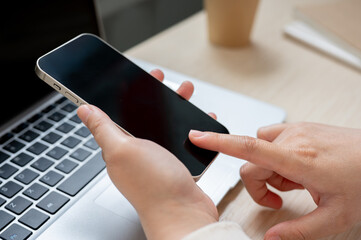 A close-up image of a woman using her smartphone at her office desk, checking messages.