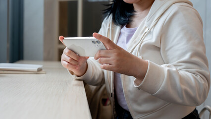 A woman holding her smartphone in a horizontal position, watching videos while sitting in a cafe.