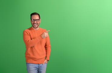 Portrait of cheerful salesman pointing at empty space and marketing new product on green background