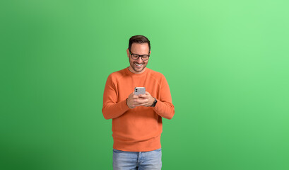 Portrait of handsome entrepreneur smiling and messaging online over smart phone on green background