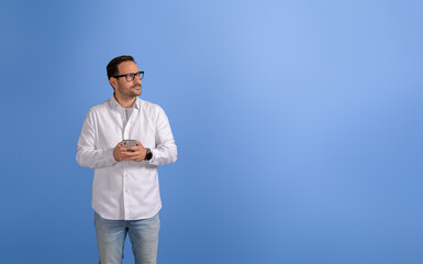 Thoughtful young businessman with mobile phone looking away seriously over isolated blue background