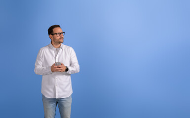 Thoughtful young businessman with mobile phone looking away seriously over isolated blue background
