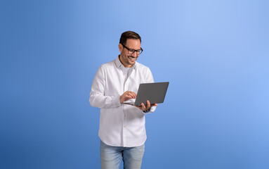 Portrait of handsome entrepreneur checking e-mails over wireless computer on blue background