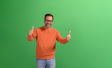 Portrait of successful male manager showing two thumbs up signs and laughing on green background