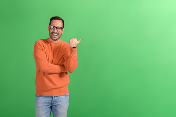 Portrait of ecstatic handsome salesman pointing at copy space and marketing over green background