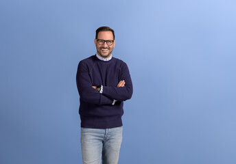 Confident male entrepreneur with arms crossed smiling at camera and standing over blue background