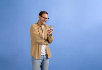 Portrait of smiling handsome manager checking online messages over mobile phone on blue background