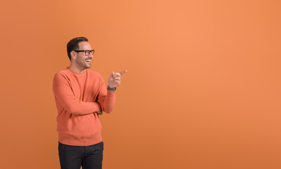 Happy young businessman pointing at empty space and demonstrating new product on orange background
