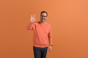 Portrait of handsome ecstatic manager showing OK sign and laughing on isolated orange background