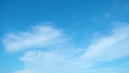 A bright blue sky with a few wispy white clouds scattered across it. The clouds have a soft, fluffy appearance, creating a serene and peaceful atmosphere. Blue sky background.
