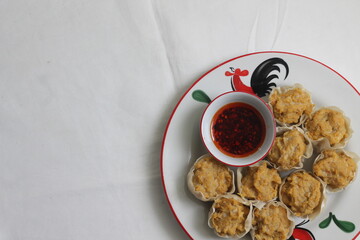 Chicken dumplings and a bowl of chilli oil on white plate decorated with cocks drawing or ayam jago in Indonesia. On white tablecloth. Selective focus