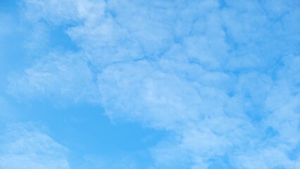 A clear blue sky with a pattern of fluffy, white clouds. The clouds are densely packed, creating a textured, almost quilt-like appearance against the vibrant blue backdrop. Cloud background.
