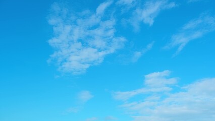 A bright blue sky dotted with scattered white clouds. The clouds are thin and wispy, spread across...