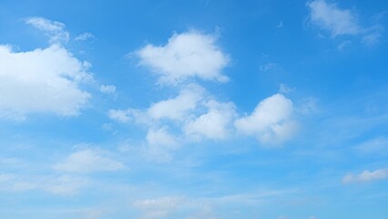 A bright blue sky scattered with fluffy white clouds. The clouds vary in size and shape, creating a...
