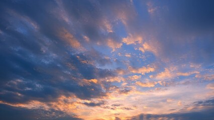 A dramatic sunset with a sky full of clouds. The clouds are illuminated with hues of orange, pink, and purple, contrasting against the darker blue and indigo areas of the sky. Cloud background.
