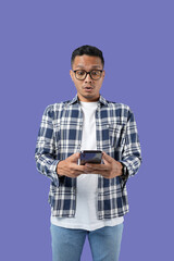 Portrait of a young cheerful excited Asian man standing isolated over a purple background, using a mobile phone