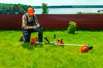 Man repair of petrol mower, checking trimmer  on the lawn. repair gasoline trimmer, repair of...